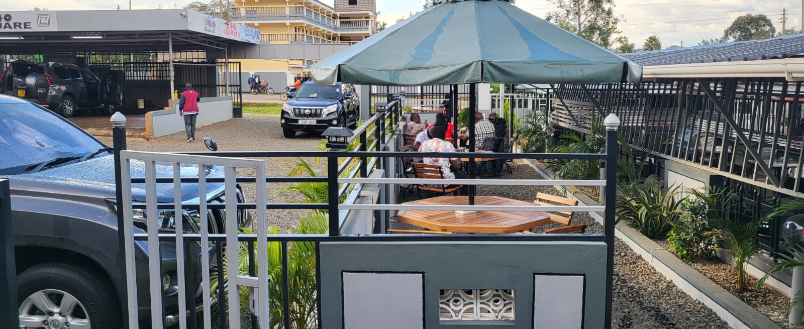 Customers seated under the umbrella in the garden at Eight Forty Square, with the car wash bays behind